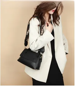 Detail of a black leather crossbody bag with a wide patterned strap on white blazer