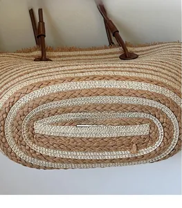 Detail view of striped woven tote bag featuring leather handle and straw tassel accent