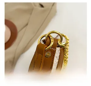 Close-up of golden metal chain and leather trim on beige woven shoulder bag