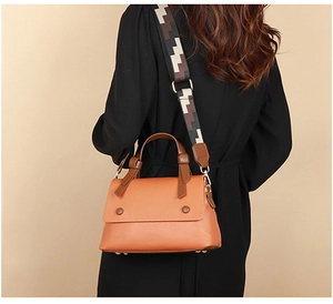 Detail of orange lychee leather handbag with geometric woven wide shoulder strap on model