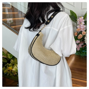 Side view of crescent straw shoulder bag with black trim and gold rivets on a model