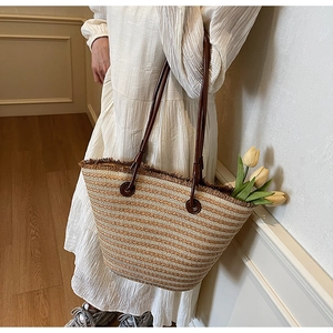 Detail of striped woven straw tote bag with brown leather straps and fringe accents