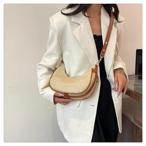 Detail of half-moon straw crossbody bag with brown leather trim and golden metal buckles