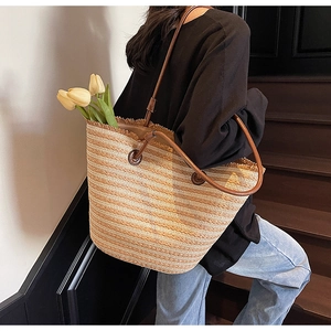 Detail of striped woven straw tote bag with fringe edge and leather strap for summer