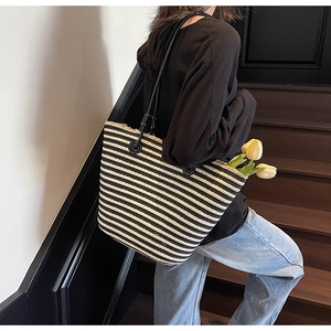 Detail of striped woven tote bag with fringe edge and black leather shoulder strap