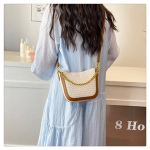 Detail of woven straw crossbody bag with brown leather trim and gold chunky chain