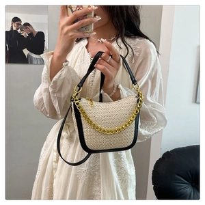 Detail of woven straw handbag with black leather trim and chunky gold chain strap