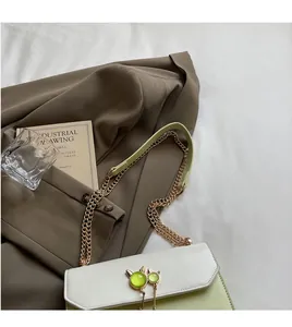 Détail du sac bandoulière vert avec décor d'oreilles de chat et chaîne dorée sur blazer