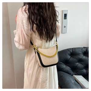 Model wearing a woven saddle bag with beige texture, black trim and gold chain detail