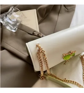 Détail du sac crème avec chaîne dorée épaisse et boucle ornée d'une pierre verte