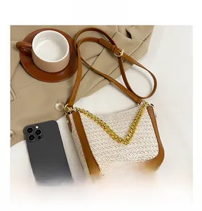 Top view of woven tote bag with brown leather trim and gold chain next to a smartphone