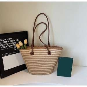Close-up of a striped straw tote bag with fringe details and slim leather shoulder straps