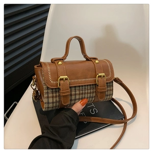 Detail of plaid retro cylinder bag with brown faux leather trim and gold buckle accents