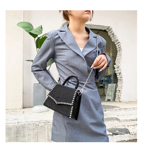 Outdoor shot of a black rhinestone chain bag worn by a model in a grey suit dress