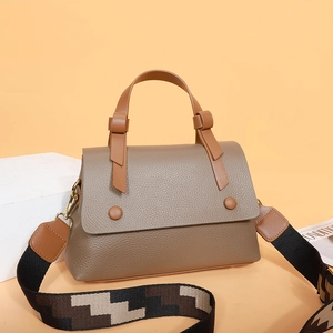 Brown lychee leather handbag with wide geometric shoulder strap on warm background