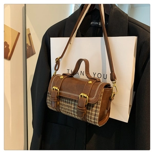 Detail of a brown plaid crossbody bag with metal buckle straps and leather patchwork