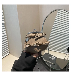 Detail of taupe litchi leather mini bag with bow accents and retro metal clasp