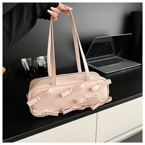 Close-up of a pink glossy handbag featuring dimensional bows on a black desk surface