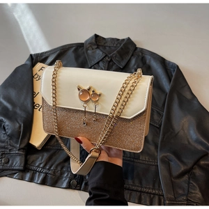 Détail du sac à chaîne bicolore en cuir crème, paillettes dorées et fermoir en forme de chat