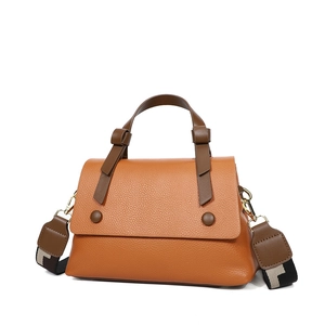 Orange lychee leather tote bag with brown buckle and geometric wide strap on white background