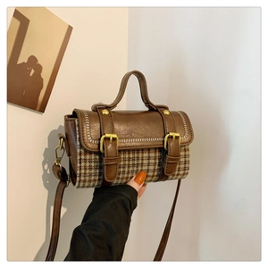 Close-up of a brown plaid handbag featuring gold rivets and leather buckle straps