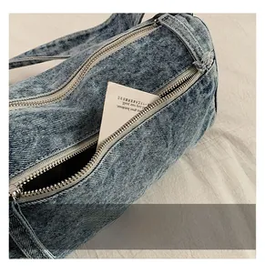 Détail du compartiment avant zippé sur un sac cylindrique en denim bleu délavé