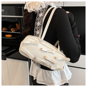 Detail of a creamy white PU shoulder bag with multiple bow accents on a model in a home setting