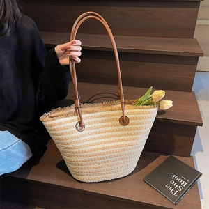 Striped woven straw tote bag with leather handles and tassel fringe on a wooden background