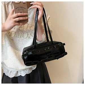 Detail of black glossy handbag with bow decorations and long handles in a mirror shot