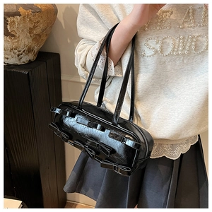 Detailed view of the black bow-accented shoulder bag with glossy finish on a fashion model