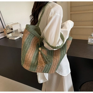 Dettaglio della borsa tote in paglia a righe con manici intrecciati e nappa colorata