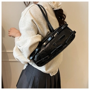 Detailed close-up of a black textured shoulder bag with chic bow accents on models arm
