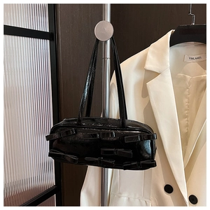Detail view of a black glossy bow shoulder bag hanging on a stylish metal stand