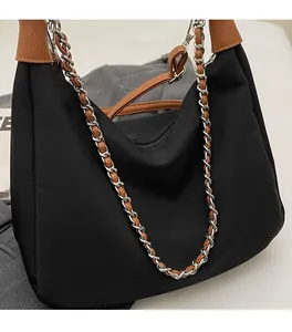 Detail of black hobo bag with brown leather trim, metal chain, and nylon texture