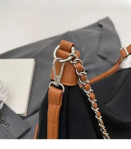 Detail of silver chain strap with brown leather trim and metallic hardware on black bag