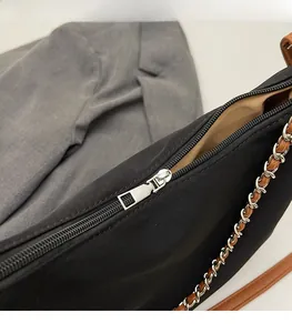 Close-up of smooth silver zipper and leather metal chain strap on a black nylon bag