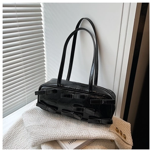 Detail showing the glossy wrinkled leather texture and black bows on the shoulder bag