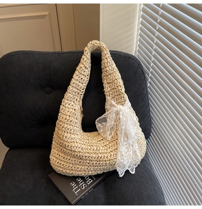 Detail of hand-woven straw shoulder bag with a large white lace bow on a black chair