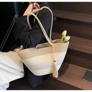 Detail of gradient woven straw tote bag with wood bead tassels on a wooden staircase