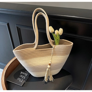 Detail of gradient straw tote bag with long tassels and wooden beads on a black chair