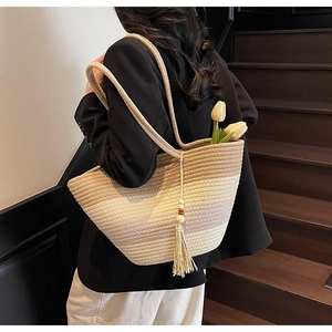 Detail of gradient woven straw tote bag featuring tassel wood bead charm and long shoulder strap