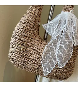 Detail of woven straw hobo bag featuring a large white lace bow and metal zipper