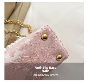 Detail of pink embroidered handbag featuring gold protective base studs and pearl handle