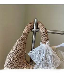 Detail of woven straw hobo bag featuring a large white lace bow on the shoulder strap