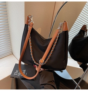 Detail of black nylon shoulder bag with brown leather strap and silver chain link