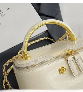 Close-up of cream glossy square bag with gold round handle and floral clasp detail