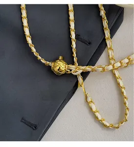 Detail of gold-tone chain strap with adjustable quilted ball buckle on white purse