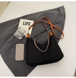 Detailed close-up of large black shoulder bag with brown leather trim and metal chain strap