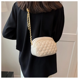 Detail of white quilted crossbody bag with gold chain strap on model's shoulder