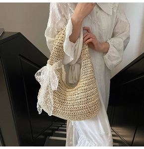 Detail of hand-woven straw hobo bag featuring a large white lace bow on the shoulder strap